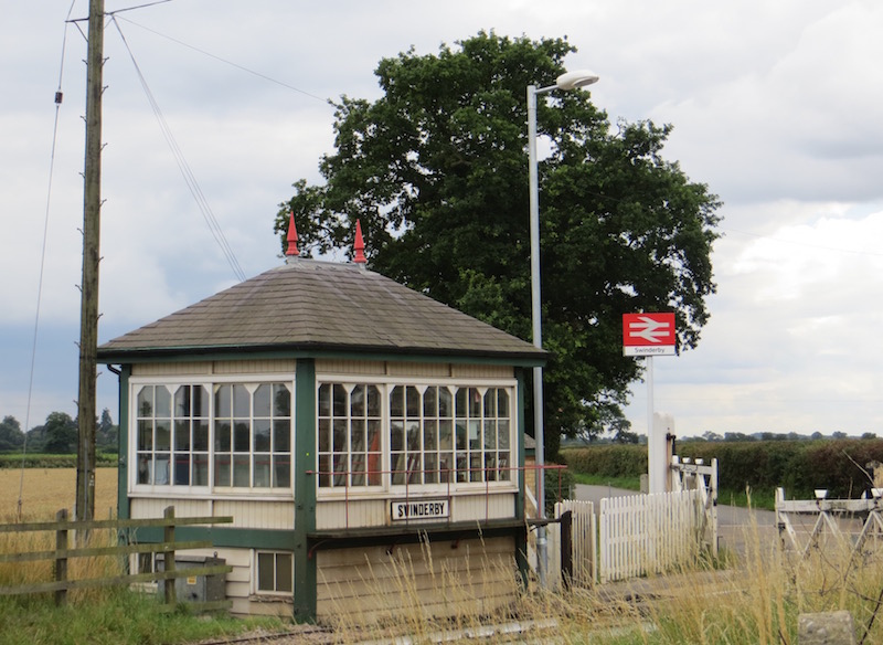 Swinderby Signal Box viewed from the front three-quarters, looking across the railway with the level crossing gates to the right